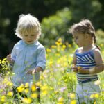 Little Boy And Girl Picking Flowers In The Parc